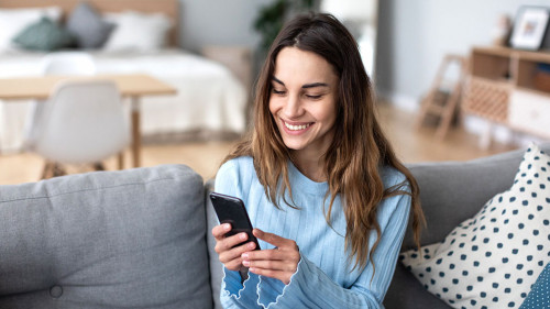 Cheerful young woman using mobile phone while sitting on a couch