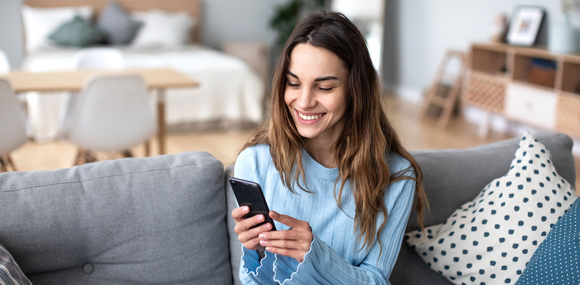 Cheerful young woman using mobile phone while sitting on a couch