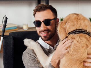 Smiling blind man sitting in armchair and hugging golden retriev