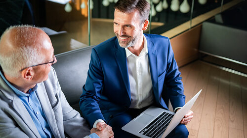 Younger and older businessman shaking hands in modern business lounge