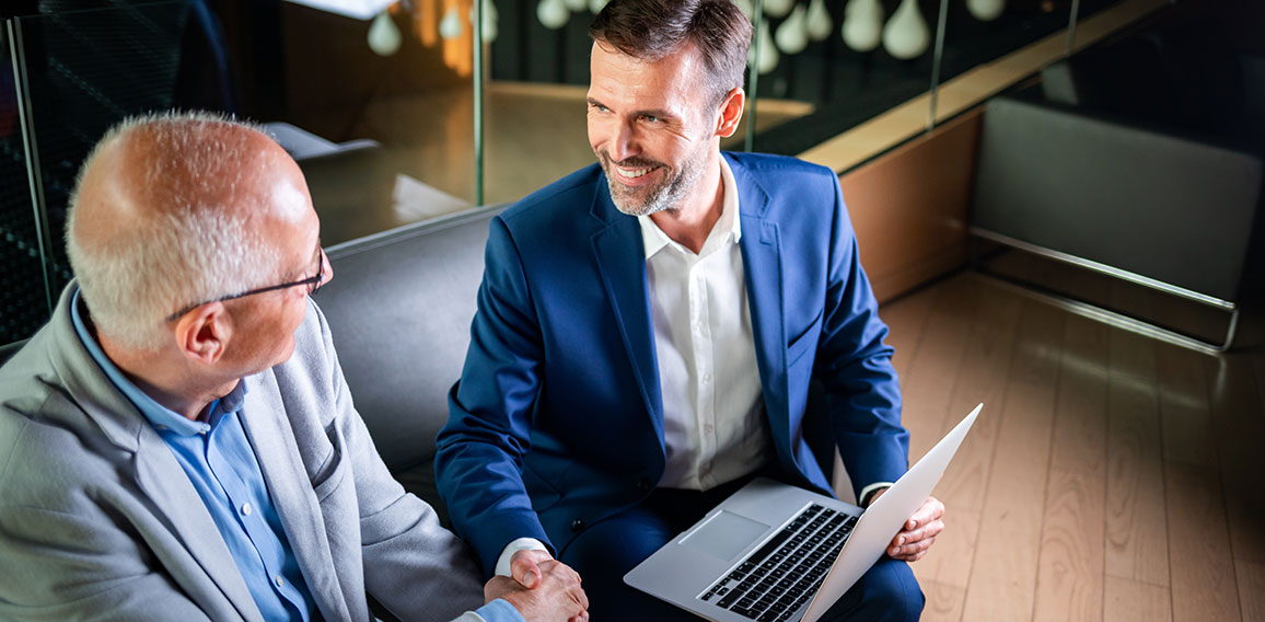 Younger and older businessman shaking hands in modern business lounge