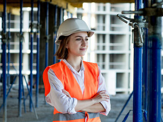 Portrait of beautiful female architect who stands idly and smiles against the background of buildings, outdoors