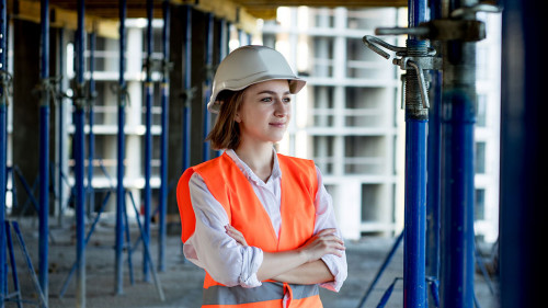 Portrait of beautiful female architect who stands idly and smiles against the background of buildings, outdoors