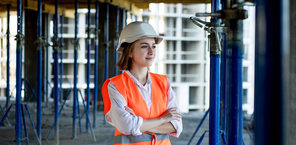 Portrait of beautiful female architect who stands idly and smiles against the background of buildings, outdoors