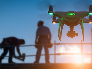 Silhouette of Unmanned Aircraft System Drone (UAV) Quadcopter Drone In The Air Over Building Under Construction.