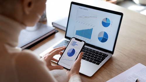 Businesswoman using smartphone and laptop, sales statistics on devices screens