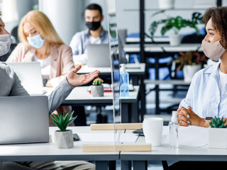 Communication and meeting in office after returning from quarantine. Young guy and african american woman in protective mask talking through glass board at workplace