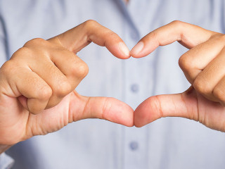 Man making heart figure love sign with fingers while standing in