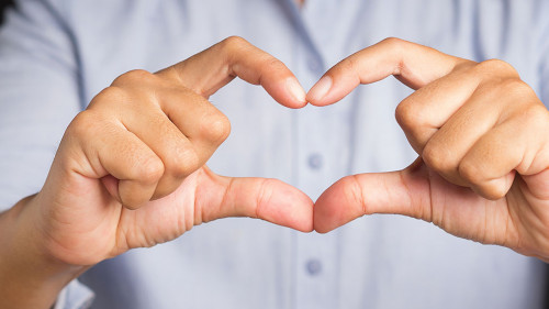 Man making heart figure love sign with fingers while standing in