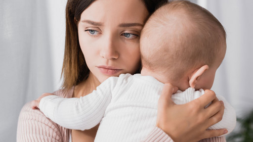 worried mother holding in arms baby boy and looking away