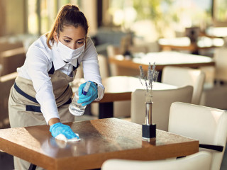 Waitress with a face mask and gloves cleaning tables with disinfectant in a cafe.