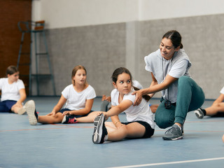Happy female PE teacher having class with group of elementary students at school gym.