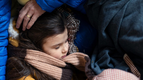Ukrainian war refugees in temporary shelter and help center, little girl sleeping on her mother's lap.