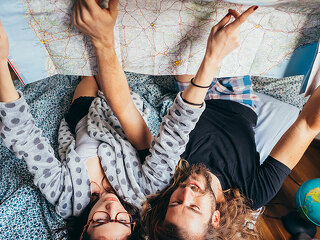 Young couple lying on bed planning travel reading map