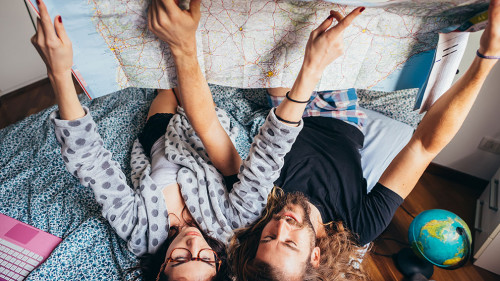 Young couple lying on bed planning travel reading map