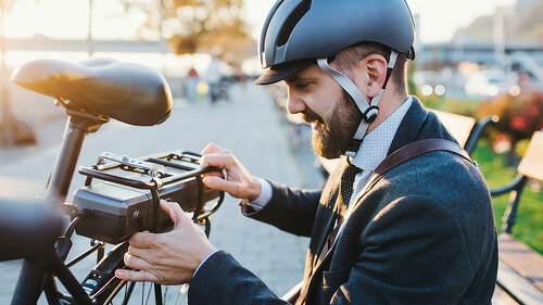 Hipster businessman commuter setting up electric bicycle in city.