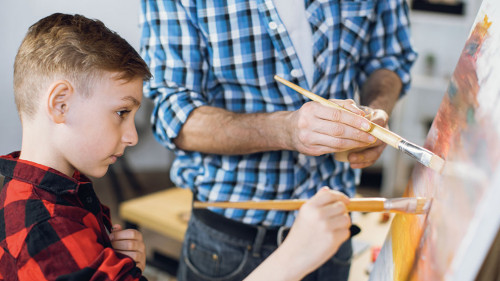 Little boy painting with father on canvas at home