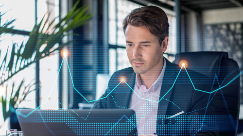 Handsome businessman in suit at workplace working with laptop to optimize trading strategy at corporate finance fund. Forex chart hologram over office background