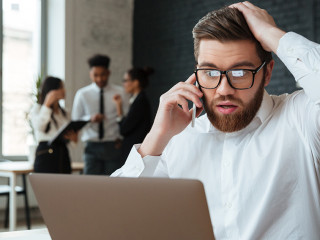 Shocked excited young caucasian businessman talking by mobile phone.