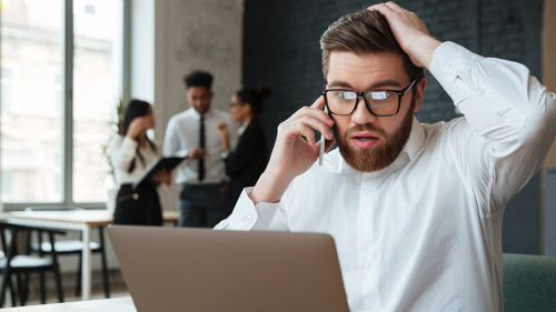 Shocked excited young caucasian businessman talking by mobile phone.