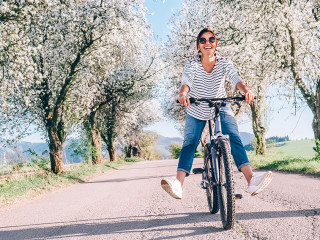 Happy smiling woman rides a bicycle on the country road under th