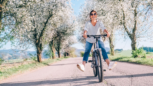 Happy smiling woman rides a bicycle on the country road under th