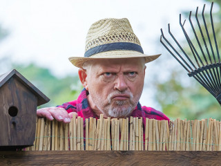 An elderly man with hat looks angry and watching over a garden f