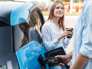 Traveling. Young couple traveling by electric car stopping at charging station boyfriend plugging in cable talking with girlfriend drinking hot coffee joyful
