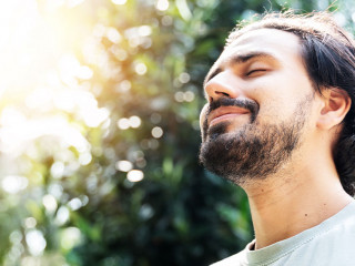 A bearded man is meditating outdoor in the park with face raised