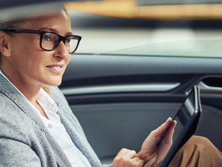 Side view of happy beautiful business woman sitting on back seat in the car and working online, she is digital tablet