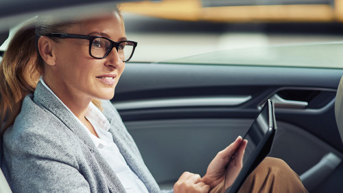 Side view of happy beautiful business woman sitting on back seat in the car and working online, she is digital tablet