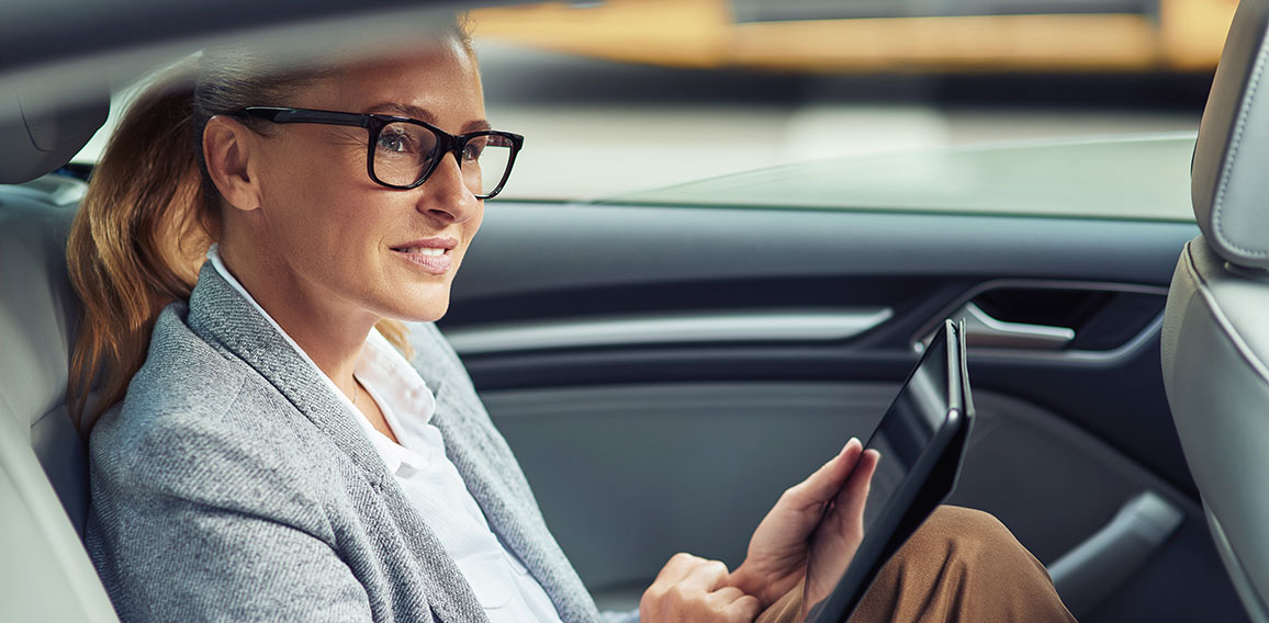 Side view of happy beautiful business woman sitting on back seat in the car and working online, she is digital tablet