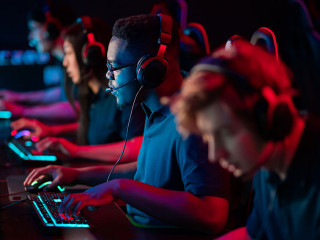A multi-racial team of esports athletes conducts a training session before an online shooter tournament. Neon light.
