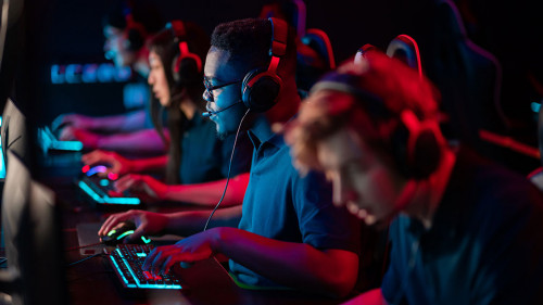 A multi-racial team of esports athletes conducts a training session before an online shooter tournament. Neon light.