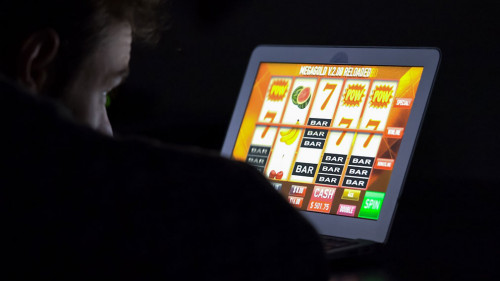 Gambling addicted man with glasses in front of online casino slot machine on laptop computer at night - loosing his money. Dramatic low light grain shot.