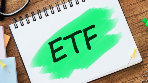 On the table are glasses, coloured markers, crumpled sheets, paper clips and a white notepad with text ETF Exchange Traded Funds highlighted in green. Business concept