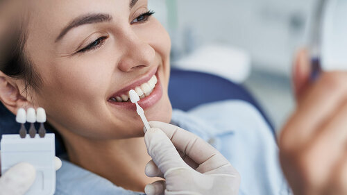 Male dentist choosing color for woman teeth