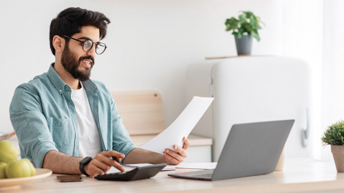 Savings and finances concept. Young arab guy using calculator and laptop computer, calculating taxes