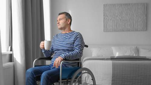 Mature man in wheelchair drinking coffee near window indoors