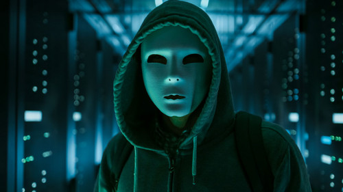 Masked Hacker in a Hoodie Standing in Corporate Data Center with
