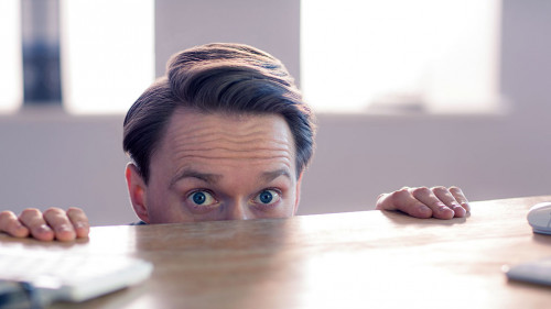 Nervous businessman peeking over desk