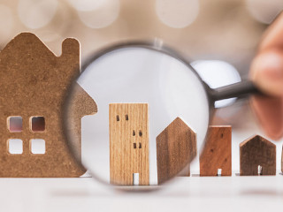 Hand holding magnifying glass and looking at house model, house
