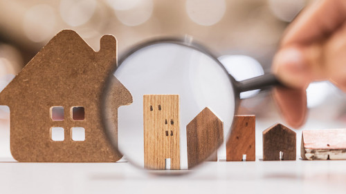 Hand holding magnifying glass and looking at house model, house