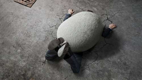 High angle view of businessman crushed by the huge stone on the