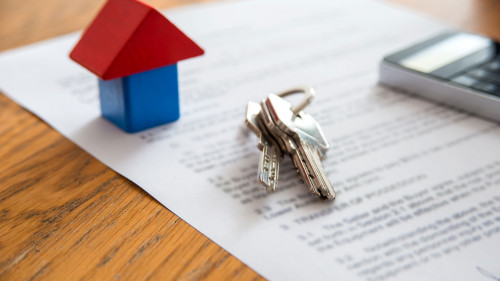Wooden house miniature and house key lying on contract