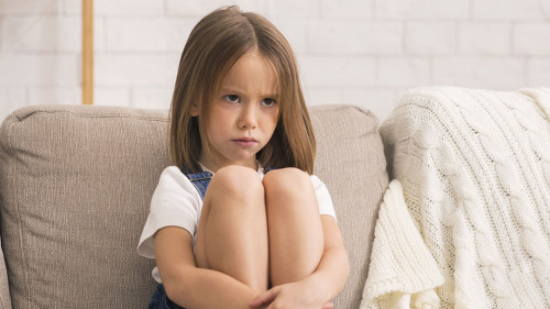 Concerned Little Girl Sitting Alone At Therapy Session With Children Psychologist
