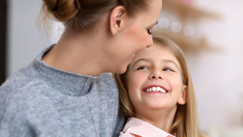 Young girl and her mother with piggybank sitting at table