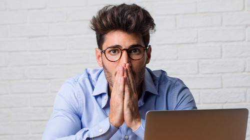 Young business man sitting and working on a laptop very scared and afraid, desperate for something, cries of suffering and open eyes, concept of madness