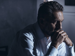 Portrait of a lonely mature man with depression sitting on a bed