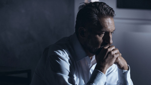 Portrait of a lonely mature man with depression sitting on a bed